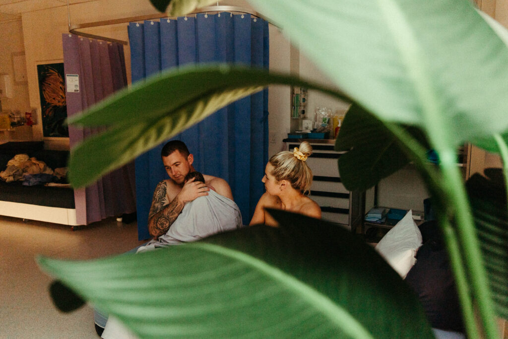 A Father and mother in the birthing suite after giving birth o their son and the father is holding the son 