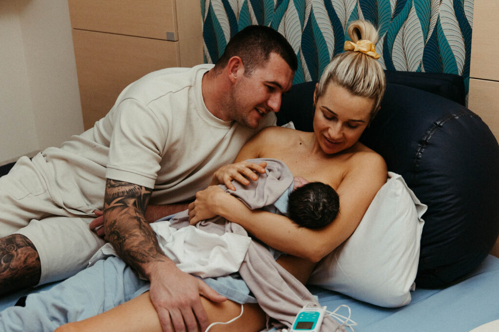 A father holding his baby and the mother of the baby after she gave birth