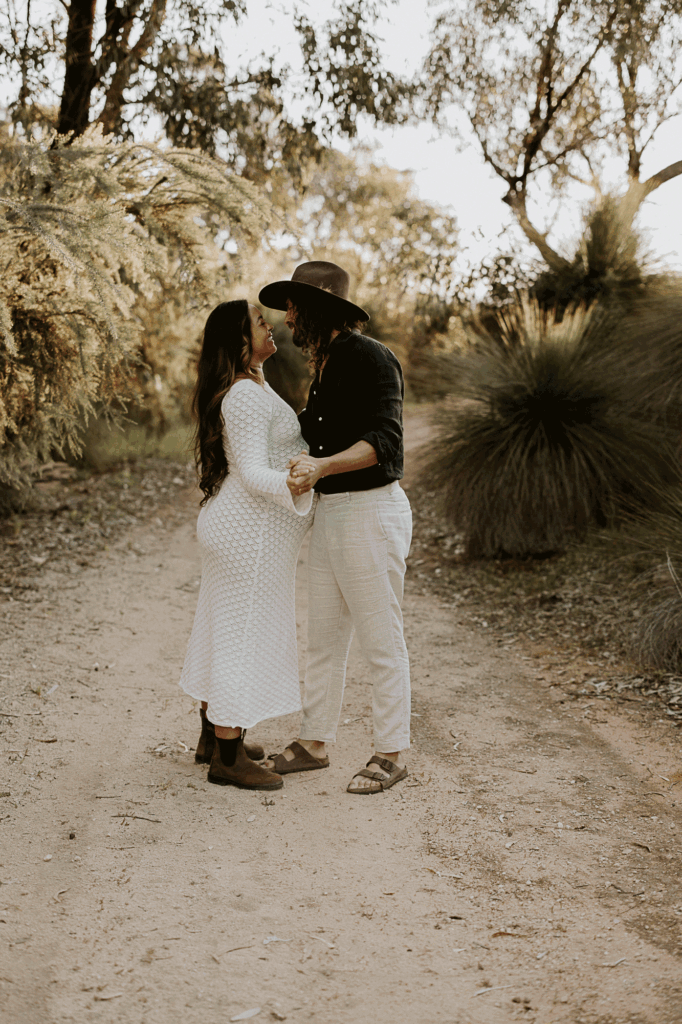 A husband and wife cuddling in the bush on a maternity shoot celebrating their pregnancy 