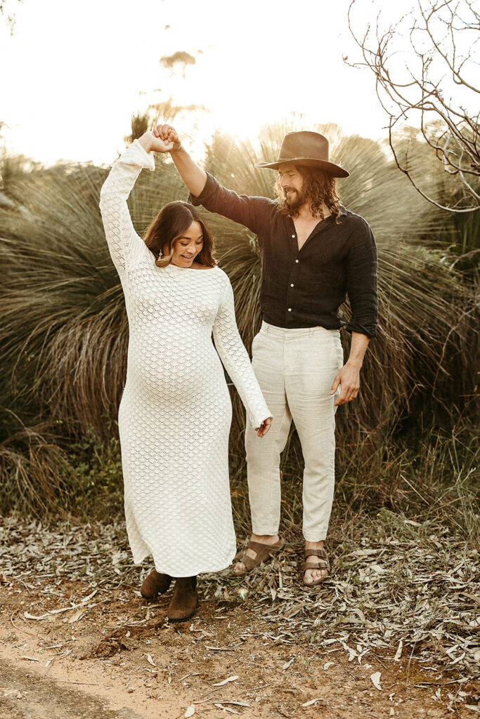 A pregnant woman and her partner holding hands in a field on a maternity photoshoot